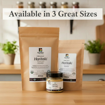 Three sizes of AyurBest Organic Haritaki Powder packaging on a wooden surface with plants in the background.